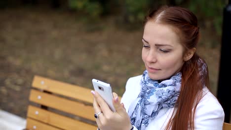 red-haired--woman-with-a-smartphone-in-her-hand-sits-on-a-bench-in-the-Park-and-communicates-in-social-networks