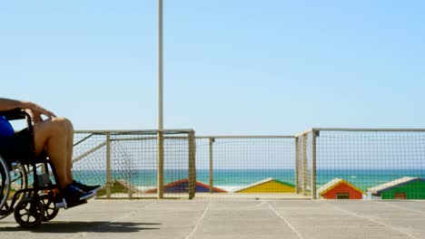 Seitenansicht-der-aktiven-Seniorkaukasschen,-die-ältere-Mann-auf-den-Rollstuhl-am-Strand-4k-drängt