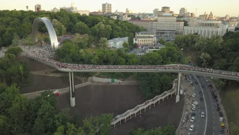 A-crowd-of-people-on-a-pedestrian-bridge-in-the-spring-evening.-Aerial-view.-A-new-bicycle-pedestrian-bridge-in-the-center-of-the-capital-of-Ukraine,-the-city-of-Kiev.-Excursions-and-walks-for-tourist