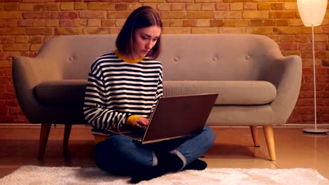 Retrato-de-primer-plano-de-joven-mujer-bonita-estudiando-en-línea-el-ordenador-portátil-sentado-en-el-suelo-en-un-apartamento-acogedor-en-el-interior