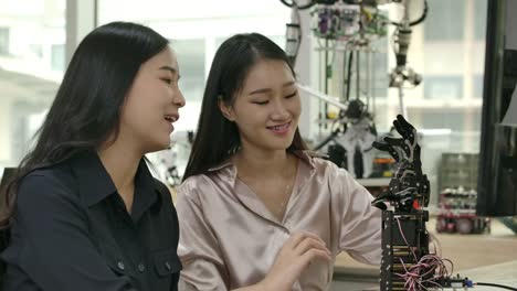 Female-electronics-engineer-building,-testing,-fixing-robotics-in-laboratory.-Two-asian-female-creates-movement-for-mechanical-robotic-hand.-People-with-technology-or-innovation-concept.