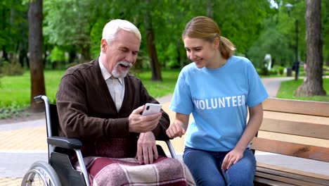 Female-volunteer-helping-disabled-old-man-use-smartphone,-nursing-home-charity