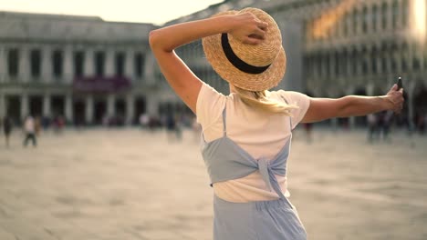 Emocionada-chica-bastante-hipster-girando-en-la-plaza-en-Roma-disfrutando-de-vacaciones-en-verano-sosteniendo-teléfono-inteligente-satisfecho-con-buena-conexión-móvil-y-4G.