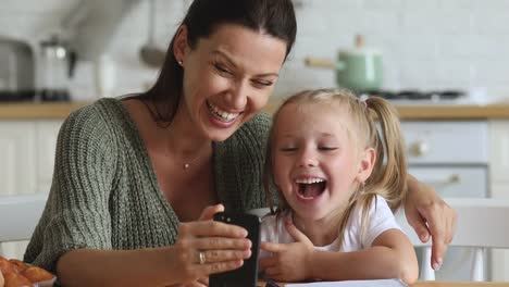 Happy-mum-and-kid-daughter-laughing-using-smartphone-at-home