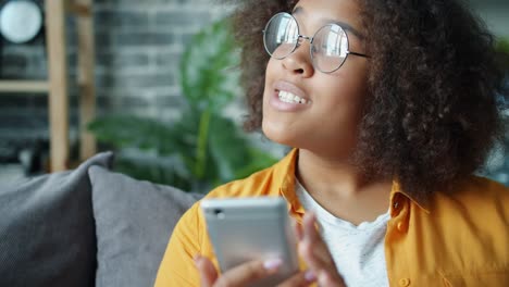 Glücklicher-afroamerikanischer-Teenager-mit-Smartphone-zu-Hause-lachen