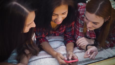 Glückliche-Freunde-liegen-auf-Decke-und-surfen-Social-Media-mit-dem-Smartphone