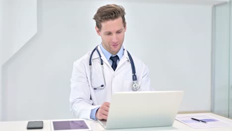 Cheerful-Young-Doctor-doing-Video-Chat-on-Laptop-in-Office