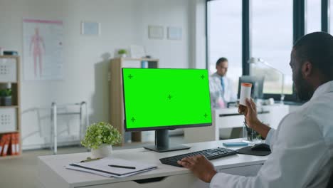 Médico-Afroamericano-está-haciendo-una-videollamada-con-el-paciente-en-una-computadora-con-pantalla-verde-en-una-clínica-de-salud.-Assistant-in-Lab-Coat-está-hablando-sobre-problemas-de-salud-en-la-oficina-del-hospital.