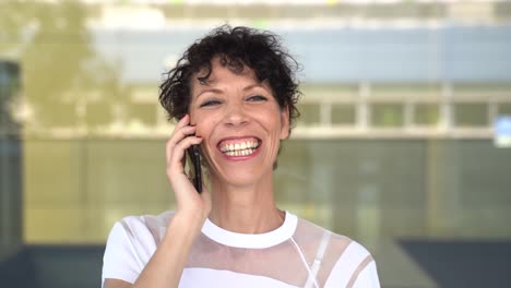 Zoom-in-close-up-shot-of-cheerful-mature-business-woman-talking-on-mobile-phone-outside-office