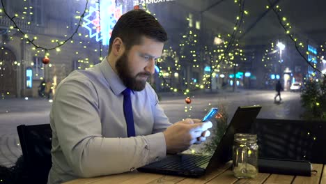 Centrado-empresario-escribiendo-en-smartphone,-en-la-noche,-en-café,-Navidad