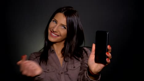 Young-attractive-woman-holding-smart-phone-in-hand-and-pointing-at-it