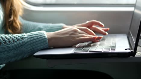 Female-hands-typing-on-keyboard-of-laptop-in-train.-Woman-chatting-with-friends-during-traveling-on-railway.-Young-girl-using-notebook.-Arm-print-a-message.-Close-up