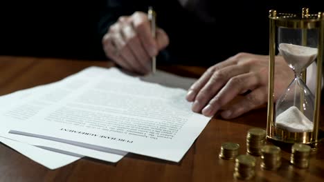 Serious-businessman-signing-purchase-agreement-as-time-flows-with-sand-in-clock