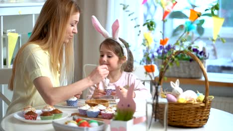 Joven-madre-y-su-hija-con-orejas-de-conejo-cocinar-cupcakes-de-Pascua