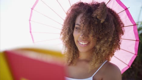 Relaxed-African-American-female-reading-book-under-sunshade