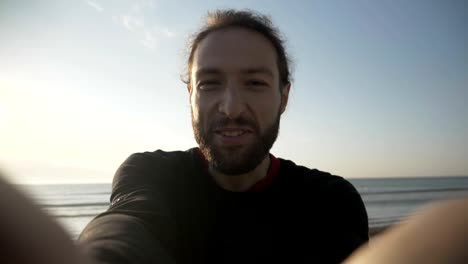 Young-man-social-media-influencer-having-fun-and-having-a-video-call-at-beautiful-sunset-on-the-beach-in-slow-motion