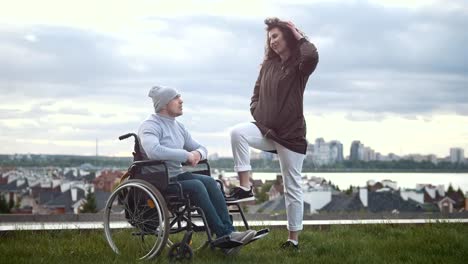 Happy-disabled-man-in-a-wheelchair-embraces-with-young-woman-outdoors