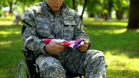 Con-discapacidad-soldado-sosteniendo-la-bandera-americana-en-manos-sentado-en-silla-de-ruedas,-patriota