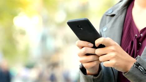 Woman-hand-texting-on-a-smart-phone-in-the-street