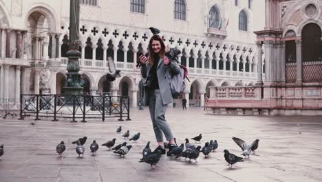 Happy-excited-attractive-tourist-woman-with-pigeons-sitting-on-her-arm-and-head-at-city-square-in-Venice-slow-motion.