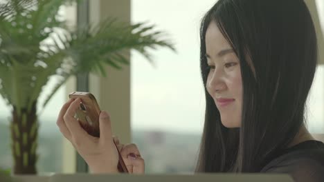 Asian-woman-sitting-at-home-typing-on-cellphone