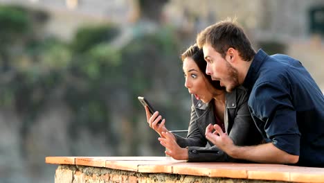 Surprised-couple-checking-phone-content-in-a-balcony