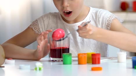 Excited-girl-taking-colored-egg-from-glass-with-red-food-coloring,-Easter-magic