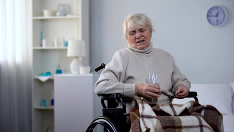 Elderly-lady-in-wheelchair-suffering-from-pain-taking-medications,-nursing-home