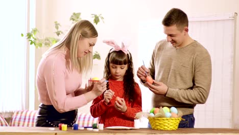 the-girl-holds-an-Easter-egg,-and-mom-and-dad-draw-on-it.