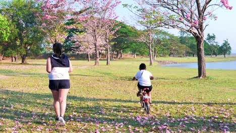 An-Asian-woman-jogging-in-natural-sunlight-in-the-evening,-along-with-his-son-riding-a-bicycle.--exercising-for-good-health.