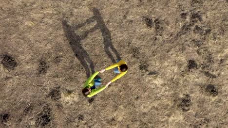 Aerial-4k-view-of-two-girlfriends-holding-hands,-rotating-in-a-meadow-by-drone