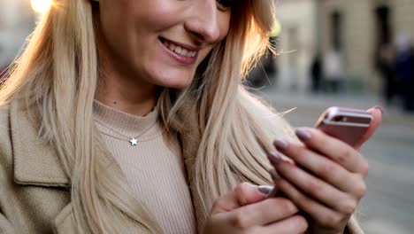 Close-up-portrait-of-woman-in-autumn-clothes-and-sun-glasses-writing-message-on-her-smartphone-outdoors.-Girl-using-digital-gadget,-scrolls-through-social-media-and-reading-new-on-device,-at-sunset.