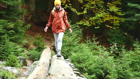 Chica-delgada-caminando-a-lo-largo-de-un-tronco-a-través-de-un-río-de-montaña-en-el-bosque