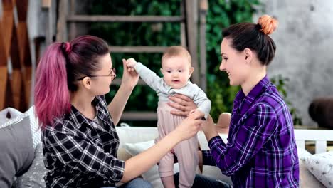 Misma-familia-pareja-de-sexo-sonriendo-y-jugando-con-poco-bebé-lindo-en-casa