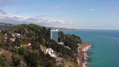 Toma-de-video-aéreo.-La-costa-del-mar-negro-de-Sochi.-Ciudad-Resort.-Hoteles-junto-al-mar.-Temporada-navideña.-Ferrocarril-a-lo-largo-de-la-costa.-Vista-panorámica-de-Adler.-Cielo-azul-claro.