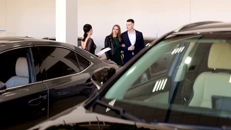 A-young-couple-in-love-buys-a-car-in-the-showroom,-they-consult-with-the-seller.