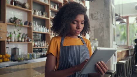 Joven-propietaria-usando-una-tableta-digital-mientras-está-de-pie-en-la-cafetería