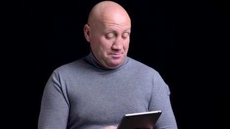 Closeup-portrait-of-adult-caucasian-man-using-the-tablet-then-looking-at-camera-and-smiling-with-background-isolated-on-black