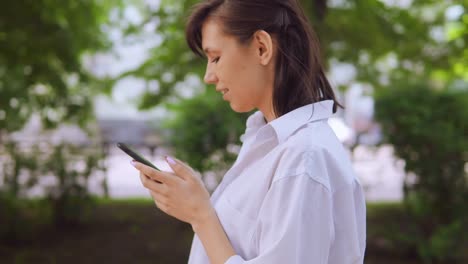 Young-female-brunette-walking-in-the-park-and-texting