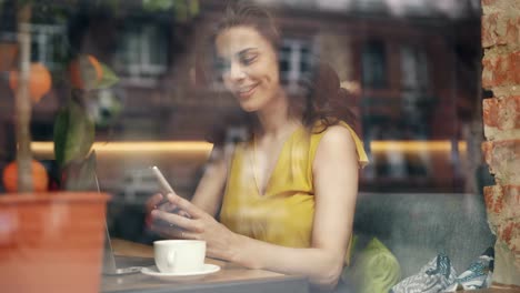 Atractiva-joven-usando-teléfono-inteligente-en-café-relajante-con-gadget-y-café