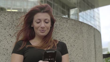 Smiling-Woman-using-smartphone-Sitting-in-business-district,-laughing-while-texting-with-mobile-telephone-outside,-typing-text-message-on-cell-phone.-Paris,-Red-hair.-Social-media.-Smiling.-4K.