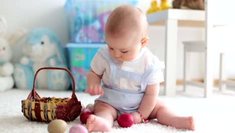 Lindo-niño-pequeño,-niño,-en-la-sala-de-estar-soleada-jugando-con-el-conejo-de-chocolate-de-Pascua-y-huevos-de-Pascua-coloridos