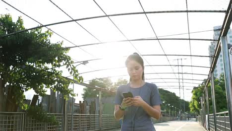 Hermosa-chica-asiática-atletas-caminando-usando-teléfonos-inteligentes-escribiendo-mensaje-de-medios-sociales-después-de-correr.-Jogging-estilo-de-vida-de-entrenamiento-en-la-calle-al-atardecer.