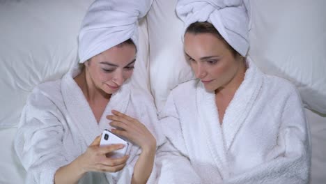 Flirty-female-friends-in-bathrobes-using-dating-app-on-gadget,-social-media