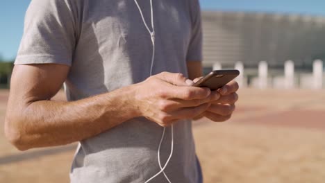 Cierre-de-las-manos-escribiendo-en-un-teléfono-al-aire-libre-en-un-día-soleado