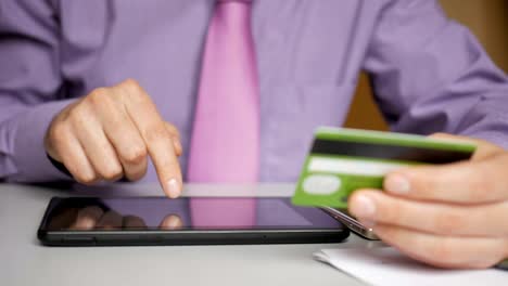 Un-hombre-de-negocios-con-camisa-y-corbata-morada-está-haciendo-un-pago-a-la-banca-por-Internet.-Compras-online-con-tarjeta-de-crédito-en-tablet-digital.