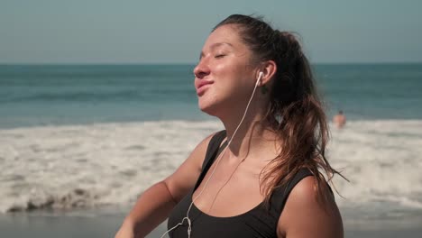 Sportswoman-listening-to-the-music-at-sandy-coastline-of-ocean