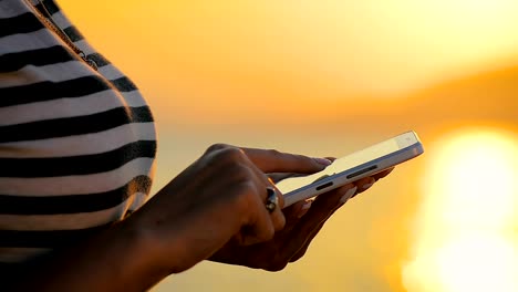 Close-up-woman-hands-using-Smartphone-in-a-trip-by-the-sea-on-the-sunset.