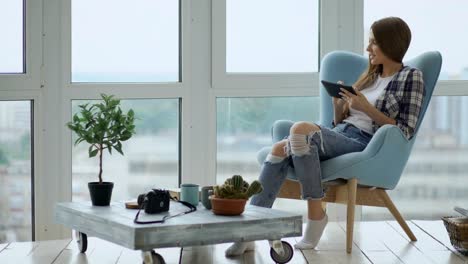 Attractive-woman-using-digital-tablet-sitting-in-chair-at-balcony-in-loft-modern-apartment