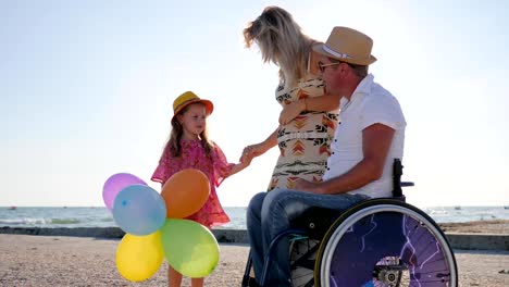 los-padres-hablan-de-persona-maternidad,-movilidad-en-silla-de-ruedas-con-familia,-niña-escucha-madre-y-padre-en-silla-de-ruedas-en-la-playa